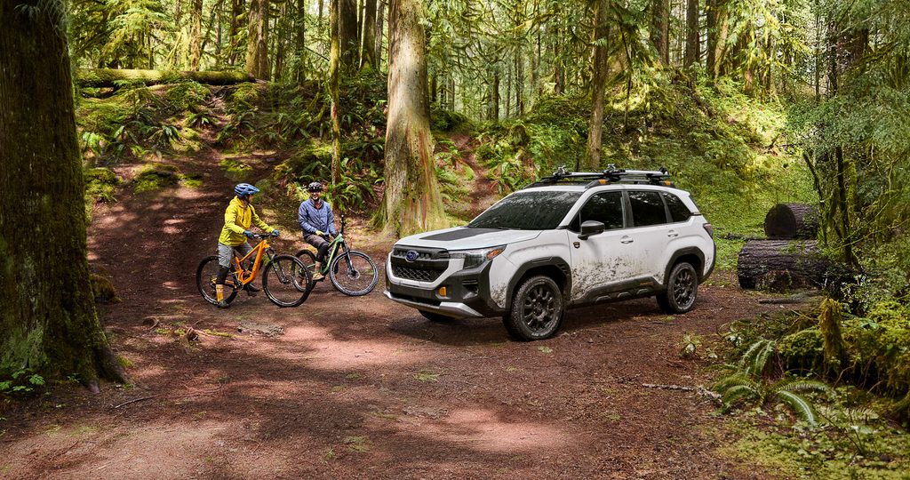 White Subaru SUV parked in a forest with mountain bikers enjoying an outdoor adventure.