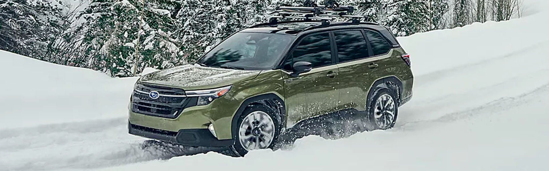 A green SUV with roof racks drives through deep snow, kicking up powder, with snow-covered trees in the background.